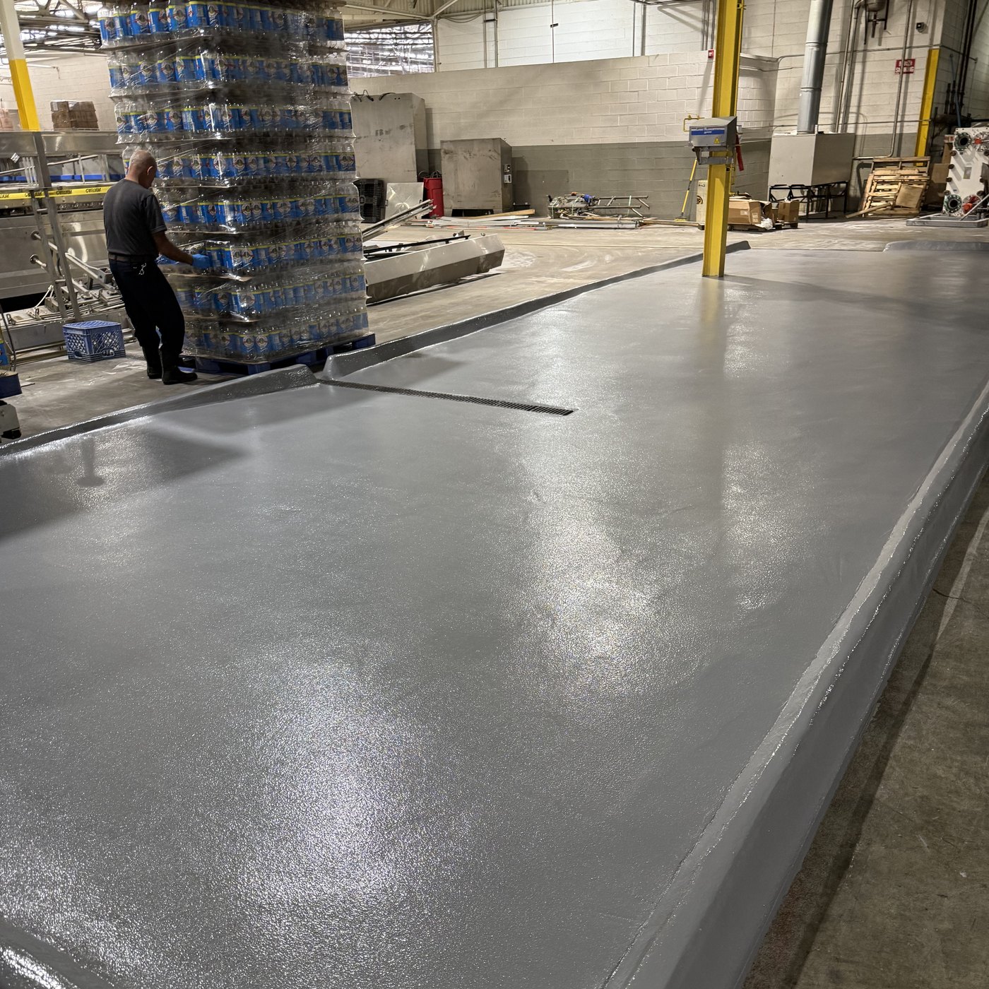 Beverage bottling plant production floor — fresh seamless gray urethane pad placed around live pallet traffic
